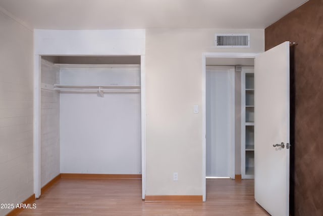 unfurnished bedroom featuring visible vents, baseboards, a closet, and wood finished floors