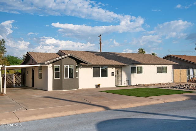 ranch-style home with stucco siding, driveway, roof with shingles, a front yard, and an attached carport