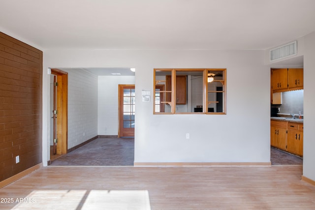 unfurnished living room featuring visible vents, brick wall, baseboards, and light wood-style floors