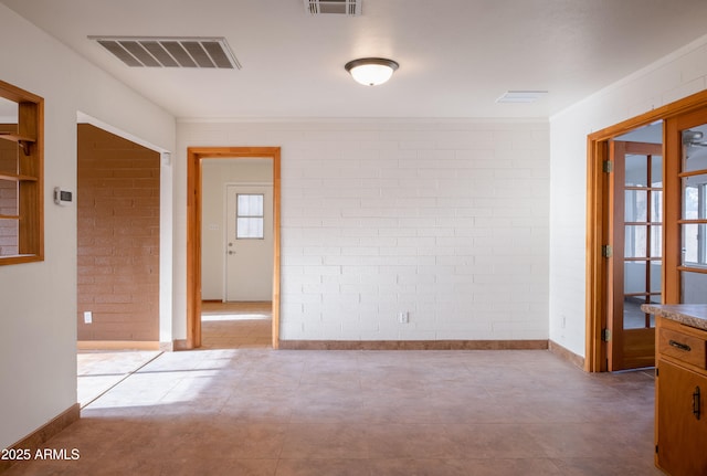 unfurnished room featuring visible vents, baseboards, and brick wall