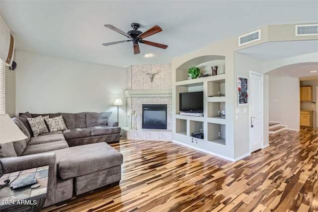 living room featuring built in features, wood-type flooring, ceiling fan, and a fireplace