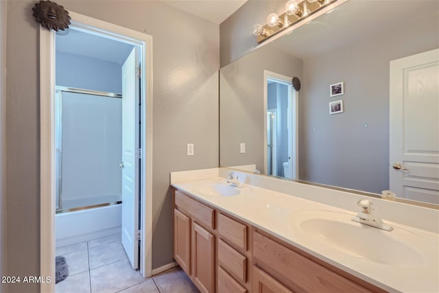 full bathroom featuring tile floors, large vanity, bath / shower combo with glass door, dual sinks, and toilet