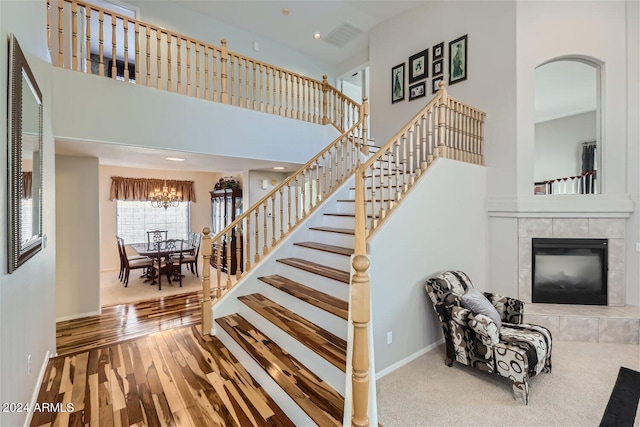 stairs with a notable chandelier, carpet, a tiled fireplace, and a high ceiling