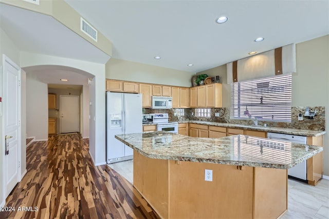 kitchen with light brown cabinets, backsplash, a kitchen island, white appliances, and light hardwood / wood-style flooring