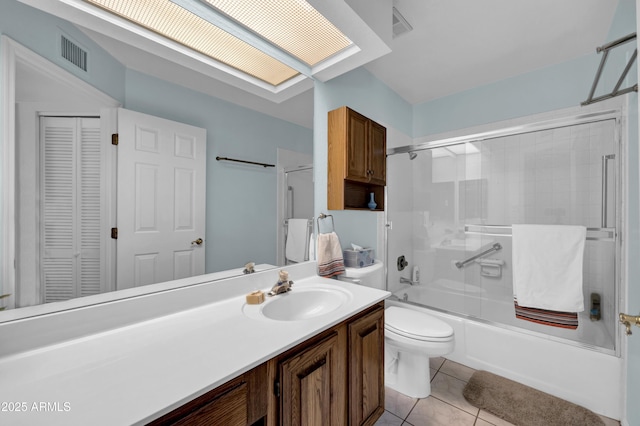full bathroom with toilet, a skylight, bath / shower combo with glass door, tile patterned floors, and vanity