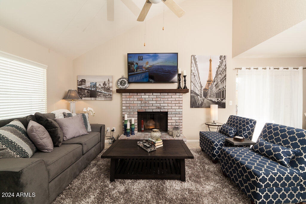 carpeted living room featuring ceiling fan, high vaulted ceiling, and a fireplace