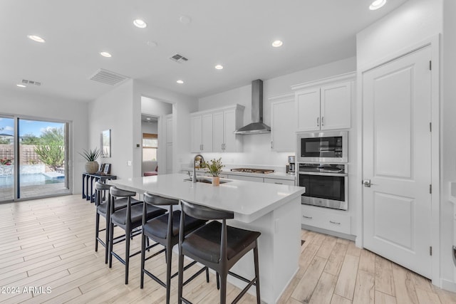 kitchen featuring a breakfast bar, a kitchen island with sink, wall chimney range hood, sink, and stainless steel appliances