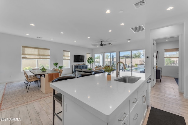 kitchen featuring light wood-type flooring, ceiling fan, sink, a center island with sink, and white cabinets