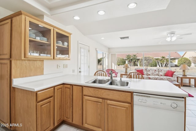 kitchen featuring light countertops, glass insert cabinets, a sink, dishwasher, and a peninsula