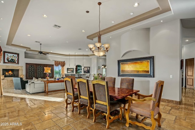 dining room with a tray ceiling, a lit fireplace, visible vents, and stone tile flooring