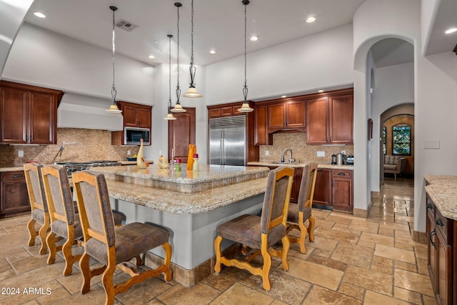 kitchen with stone tile floors, visible vents, arched walkways, built in appliances, and premium range hood