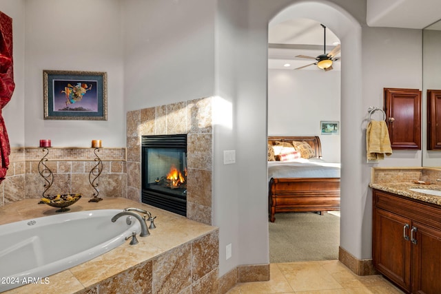 full bath featuring a garden tub, a tiled fireplace, a ceiling fan, ensuite bath, and vanity