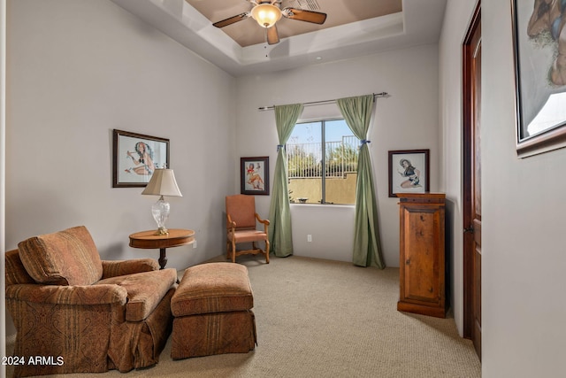 living area featuring a raised ceiling, light colored carpet, and ceiling fan