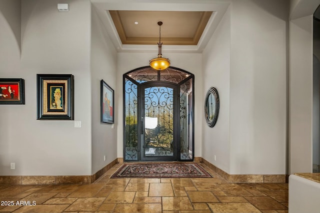 entryway with a high ceiling, a raised ceiling, baseboards, and stone tile floors