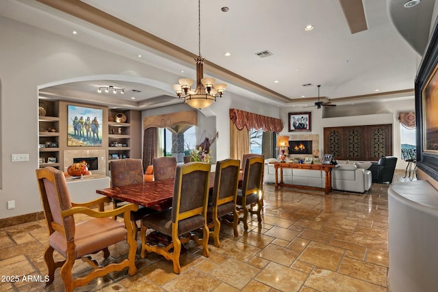 dining room with recessed lighting, a tray ceiling, a lit fireplace, and stone tile flooring