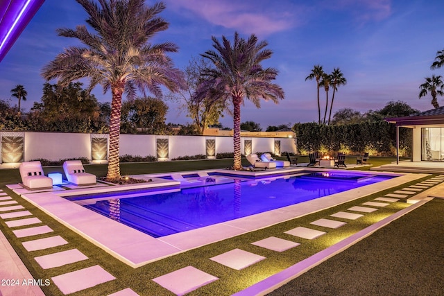 pool at dusk featuring a patio area and an in ground hot tub