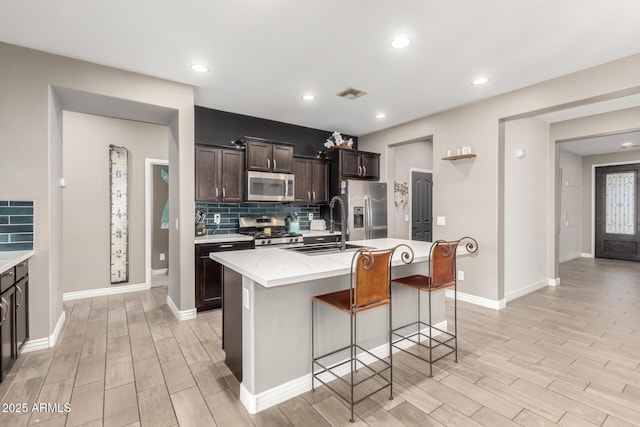 kitchen with a breakfast bar, sink, dark brown cabinetry, a kitchen island with sink, and appliances with stainless steel finishes