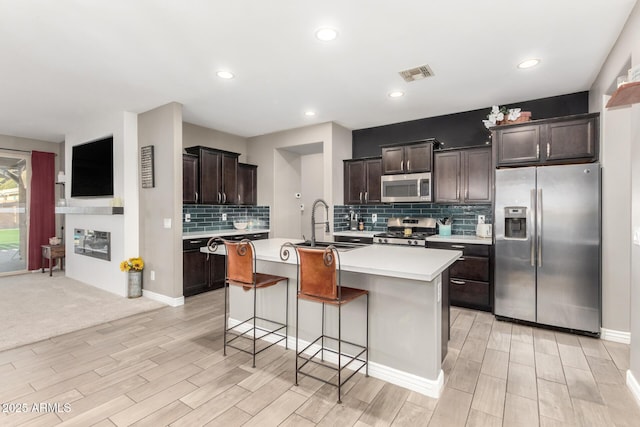 kitchen featuring an island with sink, appliances with stainless steel finishes, dark brown cabinetry, a breakfast bar, and sink