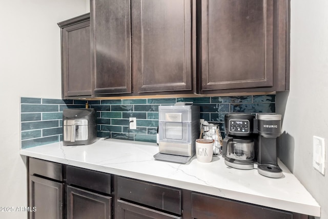 kitchen featuring decorative backsplash, light stone counters, and dark brown cabinetry