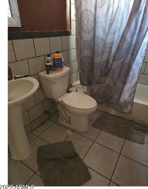 bathroom with shower / tub combo, toilet, tile patterned flooring, and tile walls