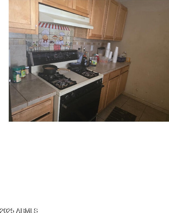 kitchen with tasteful backsplash, light tile patterned floors, range with gas cooktop, and tile counters