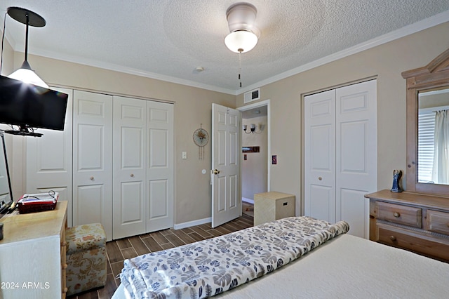 bedroom featuring a textured ceiling, crown molding, ceiling fan, and two closets