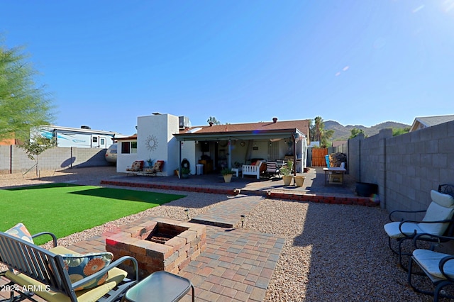 back of house featuring a mountain view, a patio area, a yard, and an outdoor living space with a fire pit