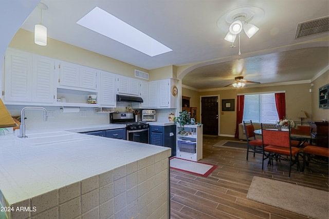 kitchen with kitchen peninsula, stainless steel range with gas cooktop, white cabinets, and hanging light fixtures