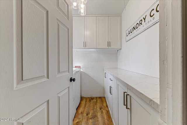 clothes washing area with hardwood / wood-style floors, washer and dryer, an inviting chandelier, and cabinets