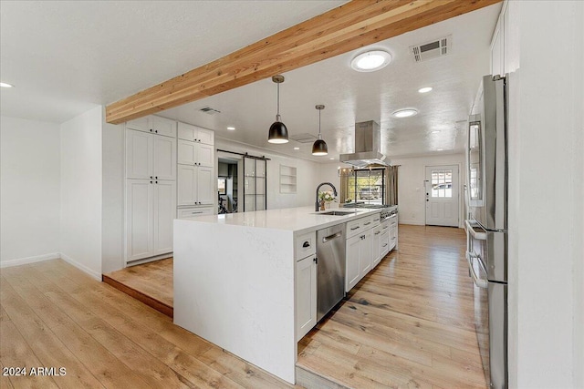 kitchen with an island with sink, appliances with stainless steel finishes, white cabinetry, a barn door, and light wood-type flooring