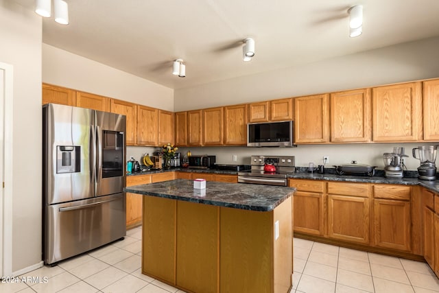 kitchen with dark stone countertops, light tile patterned floors, appliances with stainless steel finishes, and a kitchen island