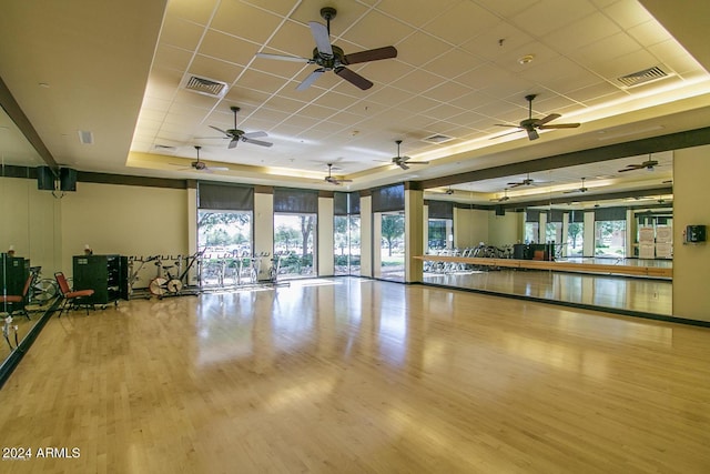 exercise room with a raised ceiling, a drop ceiling, and light wood-type flooring