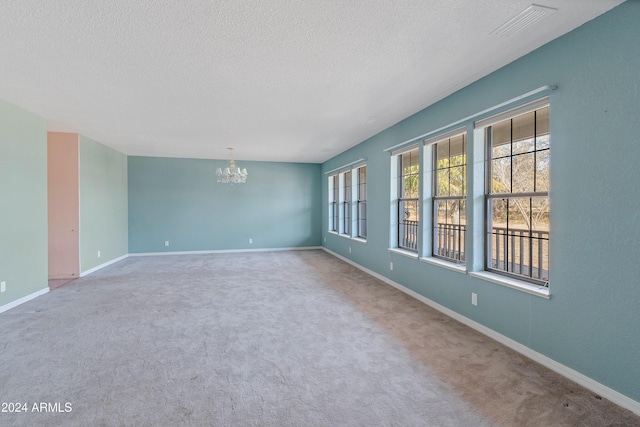 carpeted empty room with a notable chandelier and a textured ceiling