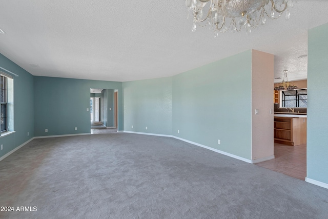 unfurnished living room featuring a textured ceiling, light colored carpet, an inviting chandelier, and plenty of natural light