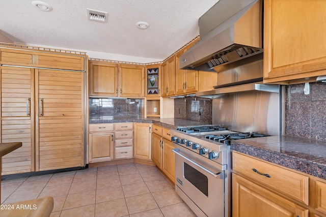 kitchen with wall chimney range hood, high end stove, a textured ceiling, decorative backsplash, and light tile patterned floors