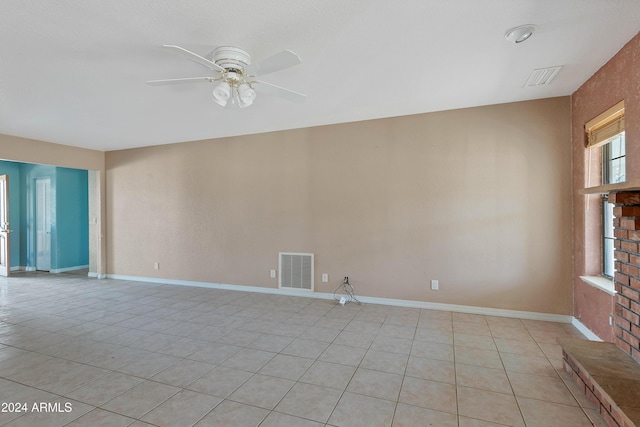 empty room featuring ceiling fan, light tile patterned flooring, and a brick fireplace