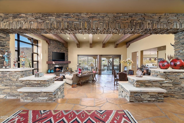 living room featuring stone finish flooring, beamed ceiling, and a stone fireplace