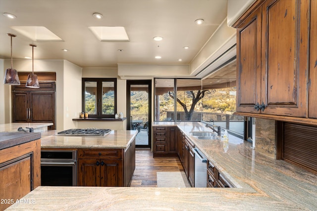 kitchen featuring light stone counters, a sink, hanging light fixtures, appliances with stainless steel finishes, and light wood-type flooring