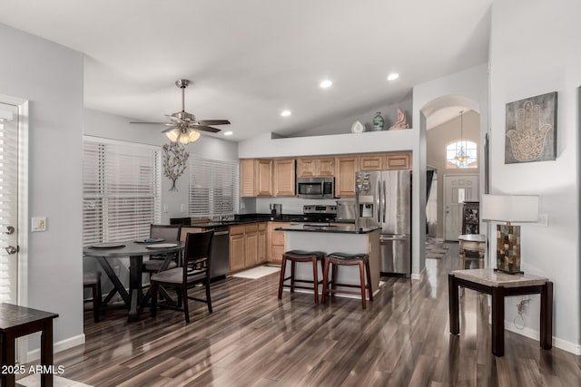 kitchen with ceiling fan, appliances with stainless steel finishes, a kitchen breakfast bar, dark hardwood / wood-style flooring, and high vaulted ceiling