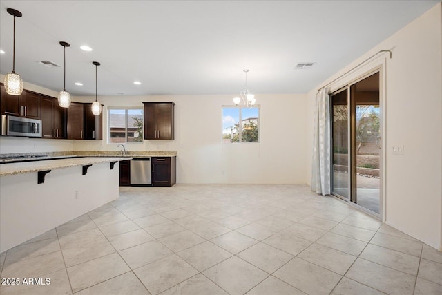 kitchen with light stone counters, dark brown cabinets, hanging light fixtures, appliances with stainless steel finishes, and a kitchen breakfast bar