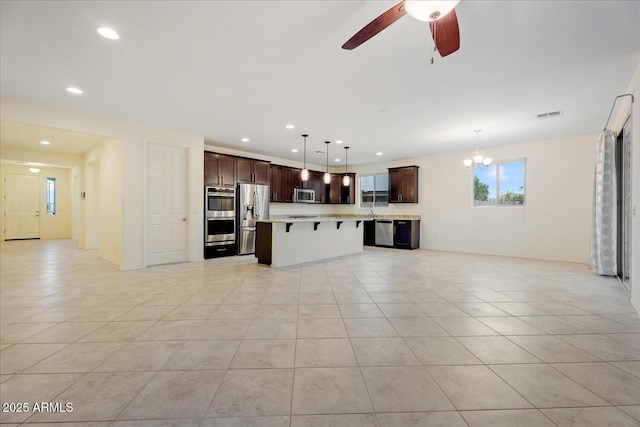 kitchen featuring dark brown cabinetry, a kitchen bar, decorative light fixtures, appliances with stainless steel finishes, and a kitchen island