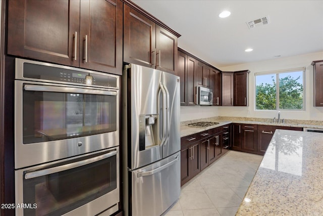 kitchen featuring light tile patterned floors, sink, stainless steel appliances, dark brown cabinetry, and light stone countertops