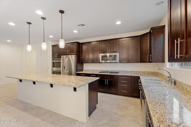 kitchen featuring appliances with stainless steel finishes, sink, a kitchen bar, hanging light fixtures, and light stone counters