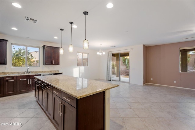 kitchen with pendant lighting, sink, dark brown cabinets, a center island, and light stone counters