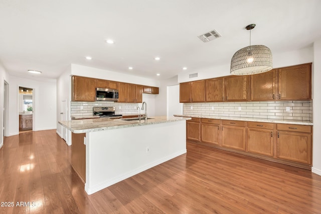 664 E Windsor Dr, Gilbert, AZ 85296 - kitchen featuring stainless steel appliances, a sink, brown cabinetry, decorative backsplash, and wood finished floors