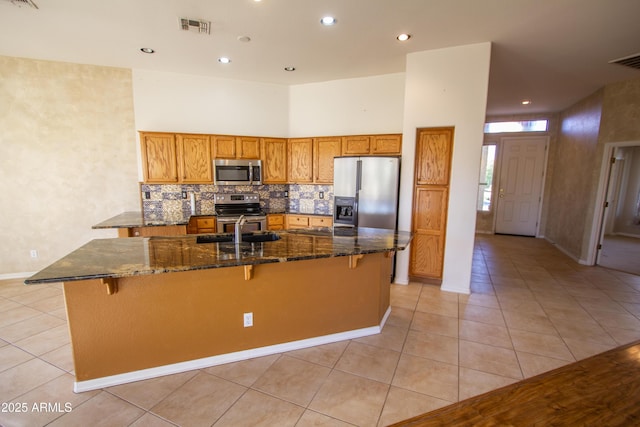 kitchen with a spacious island, a towering ceiling, appliances with stainless steel finishes, a kitchen breakfast bar, and light tile patterned floors