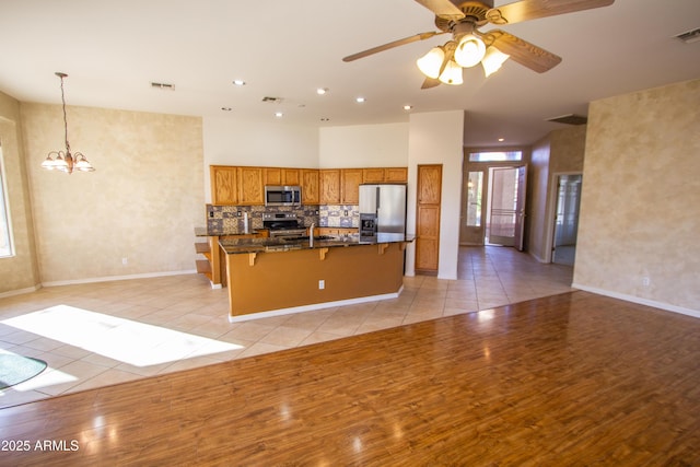 kitchen featuring appliances with stainless steel finishes, decorative light fixtures, dark stone counters, light tile patterned flooring, and a breakfast bar area