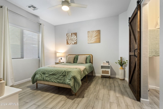 bedroom featuring a barn door, light wood-type flooring, and ceiling fan