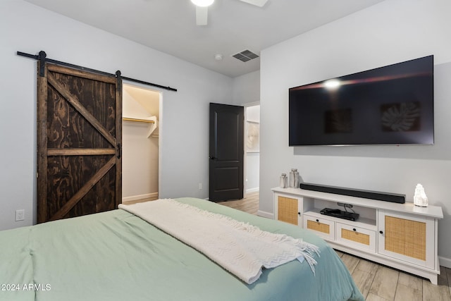 bedroom featuring ceiling fan, a barn door, light wood-type flooring, a closet, and a walk in closet