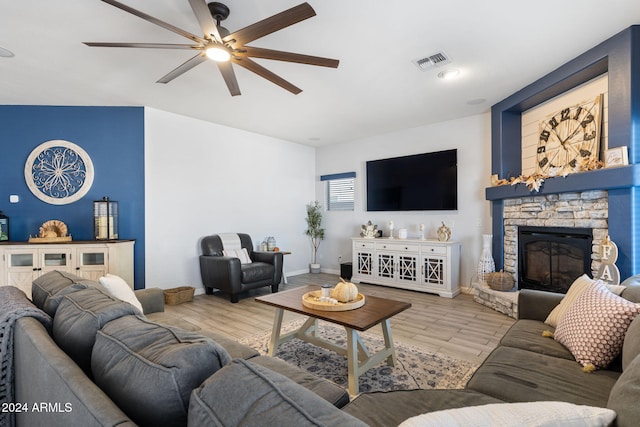 living room featuring a stone fireplace, light wood-type flooring, and ceiling fan